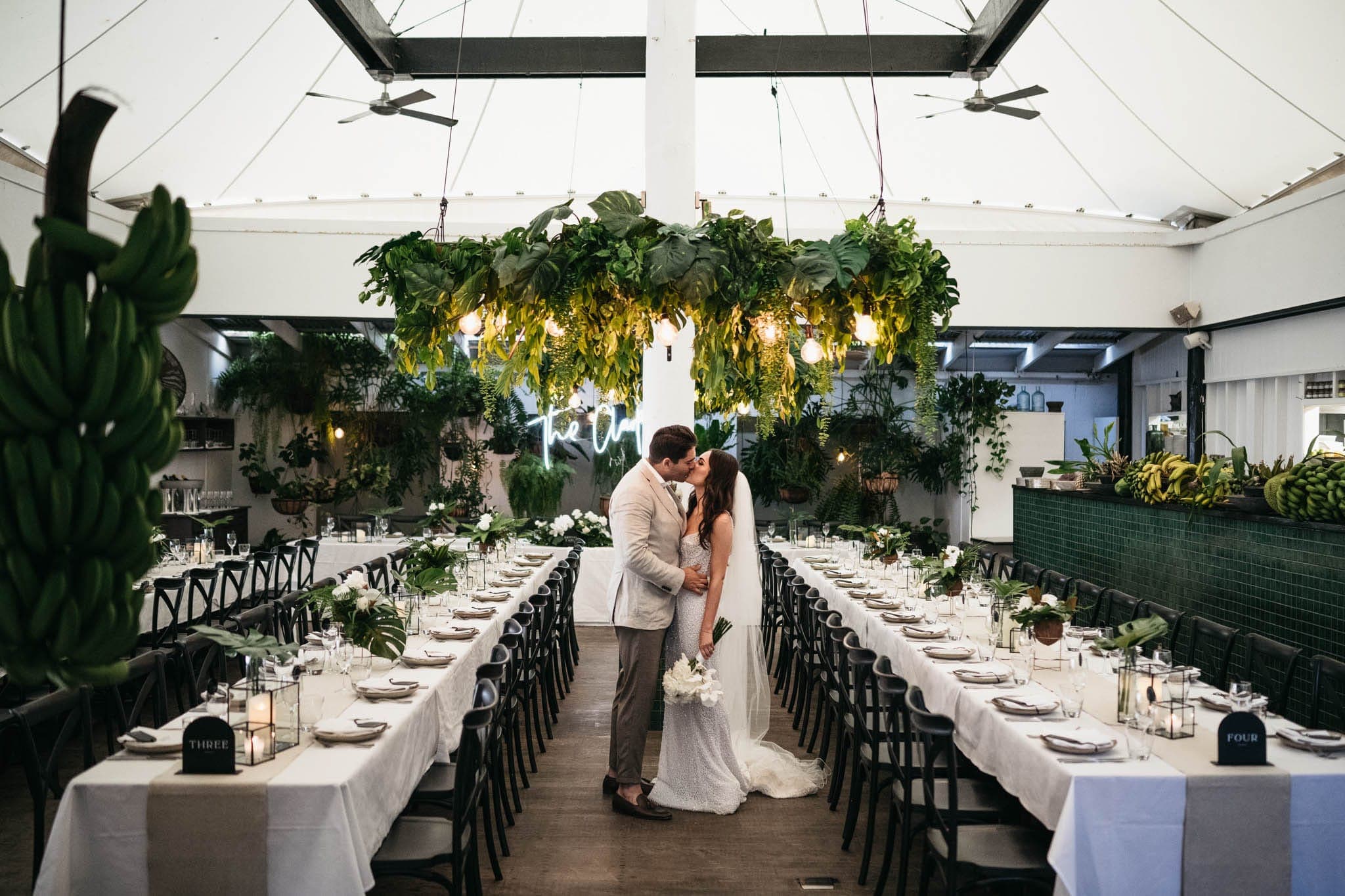 A couple kissing beneath the hanging greenery and chapel neon at a Nu Nu wedding