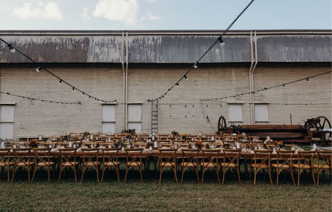 Trestle tables set for dinner the length of the mill wall, festoon lights strung overhead and an old saw carriage parked at the end