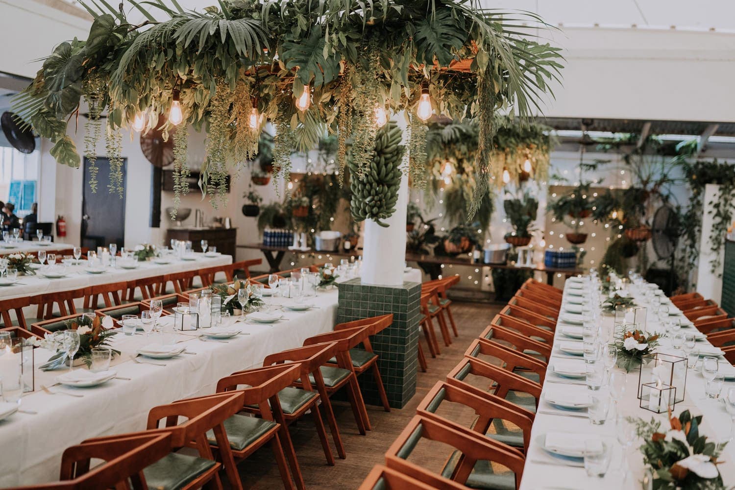 Wedding reception long tables in the Nu Nu dining room, under hanging tropical greenery and festoon light